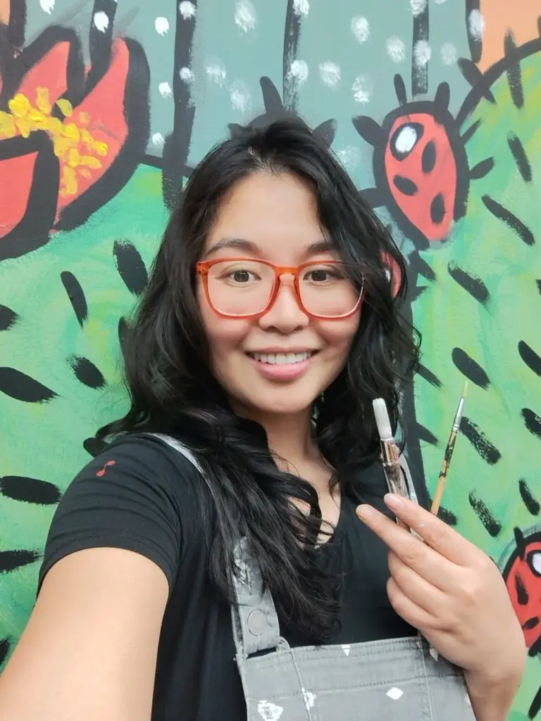 Picture of Rheazel in front of a mural she is painting